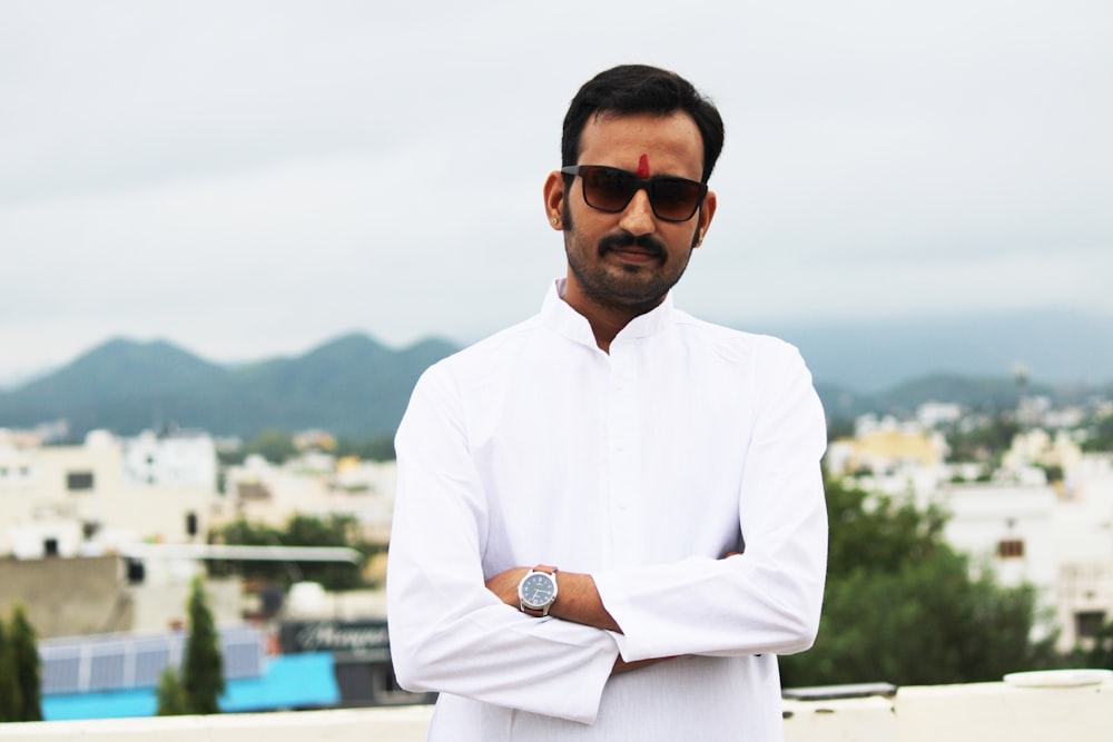 a man in a white shirt and sunglasses standing with his arms crossed