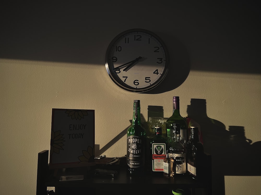 a clock on a wall above a shelf with liquor bottles