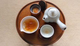 A rustic wooden tray displaying a delicate porcelain teapot surrounded by loose tea leaves and a small honey jar.