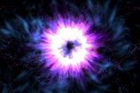 A vibrant and colorful burst of energy emanates from a central point, surrounded by swirling blue and purple hues. The intense brightness at the center contrasts with the darker outer regions, creating a sense of depth and motion.