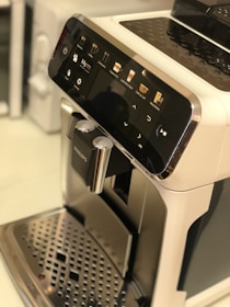 A sleek coffee machine with a user-friendly interface featuring options for various coffee types. The front panel is glossy with a digital display and several touch icons. The machine's metallic drip tray is visible at the bottom.