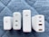 Four white charging adapters are arranged vertically on a quilted gray-blue surface. Each adapter differs slightly in design and size but commonly features USB ports, with some labeled for power delivery (PD) and specific wattages.