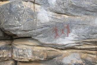 Ancient rock formation featuring prehistoric reddish-brown cave paintings depicting human figures engaged in what appears to be a dance or ritual.