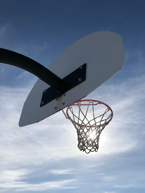 An outdoor basketball hoop with a net swaying gently in the breeze on a sunny day.