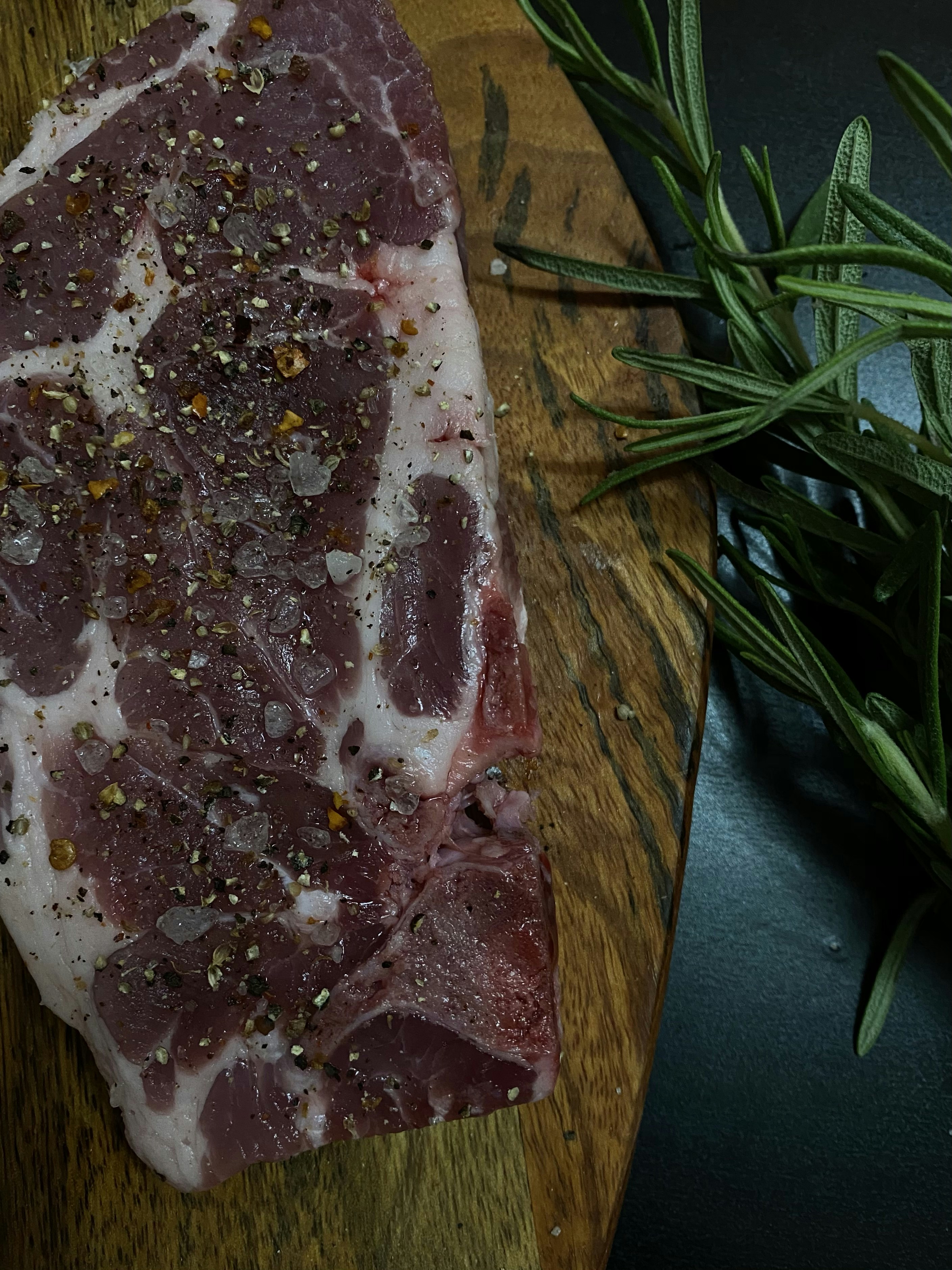Frenched lamb rack with exposed bones, fresh rosemary sprigs, dark matte background