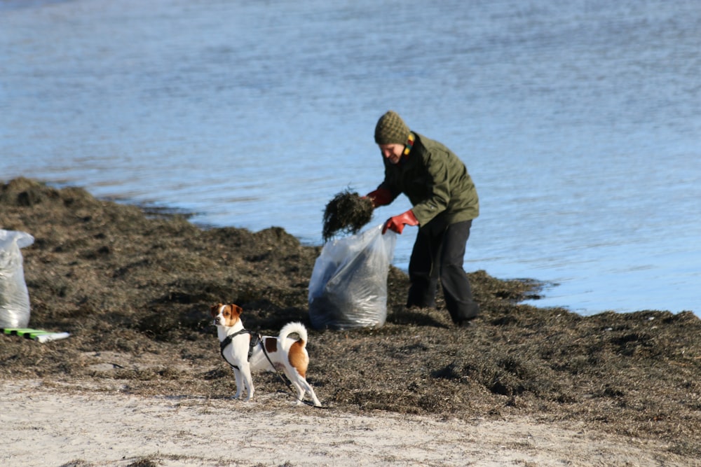 a man and a dog on a beach with a bag of garbage