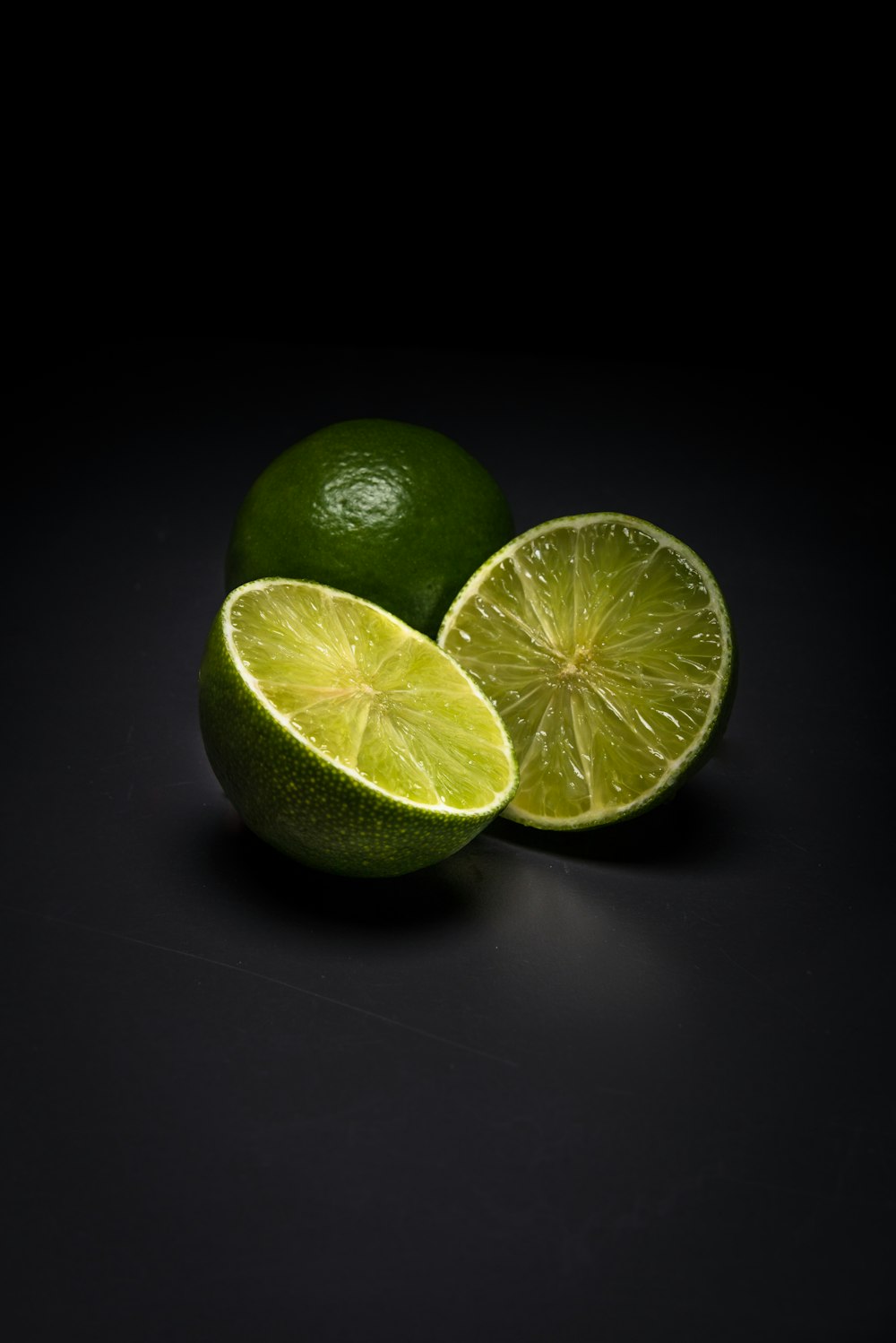 two limes with one cut in half on a black background