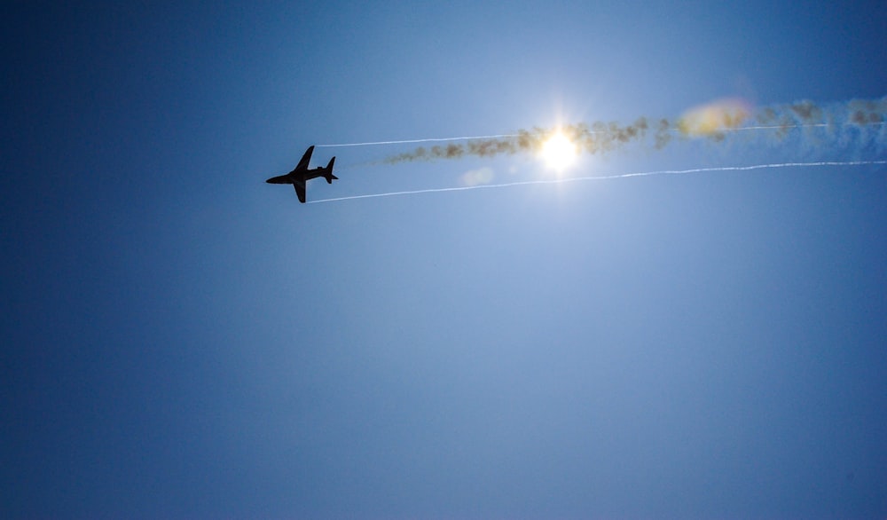 a jet flying through a blue sky with the sun in the background