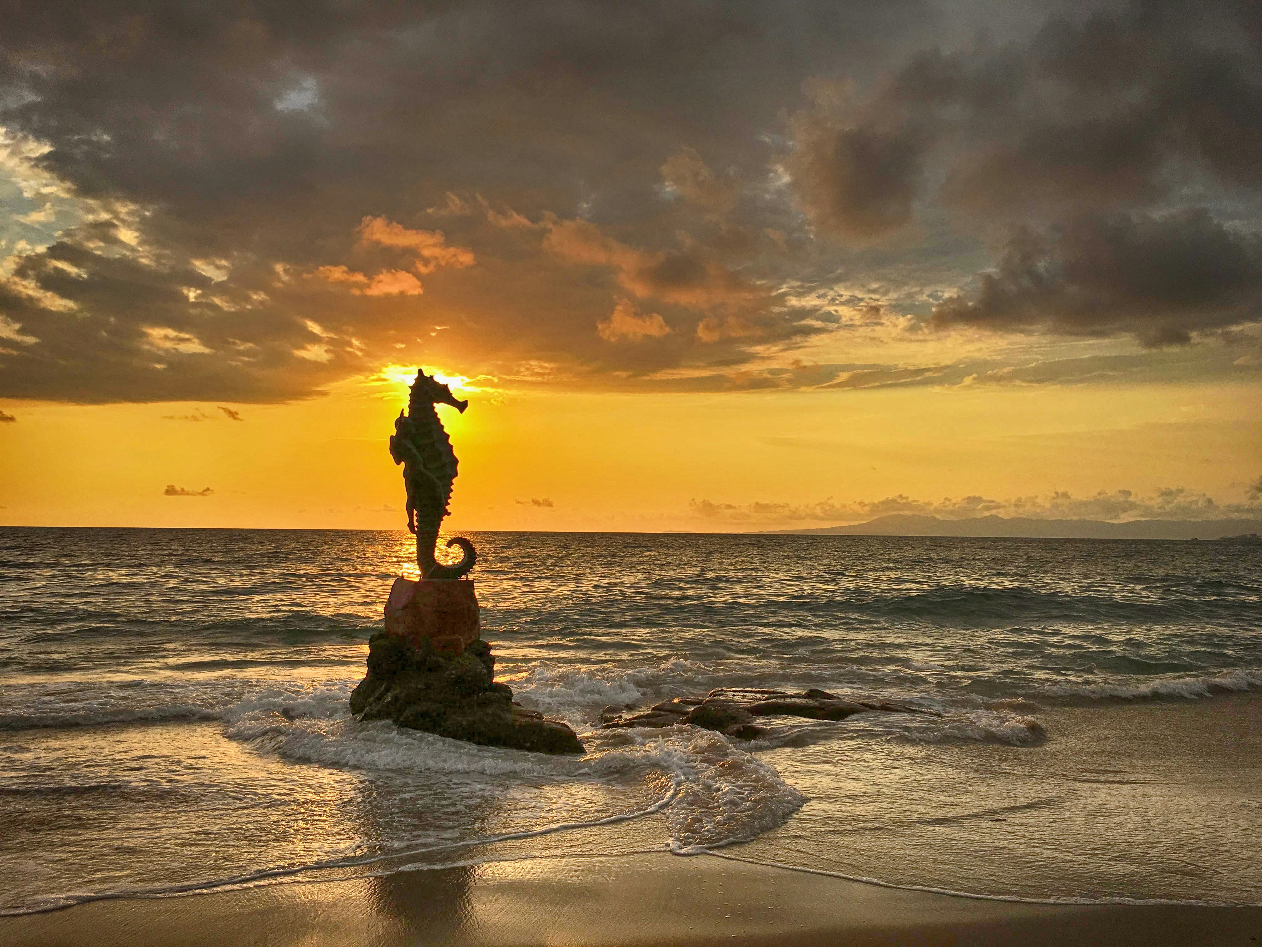 a statue of a person standing on a rock in the ocean