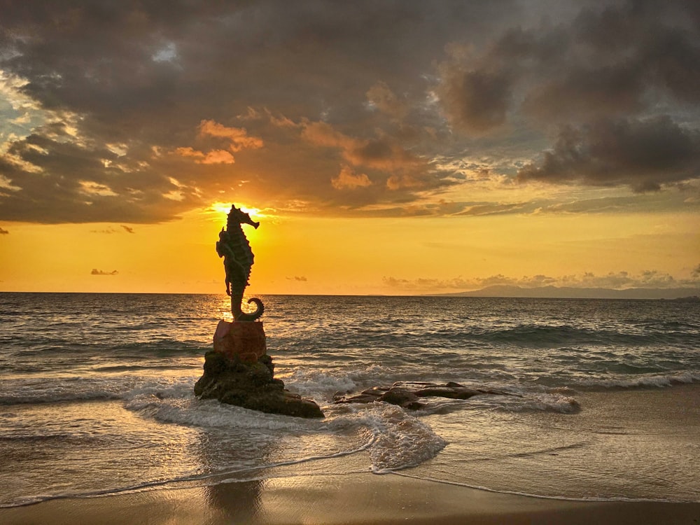 a statue of a person standing on a rock in the ocean