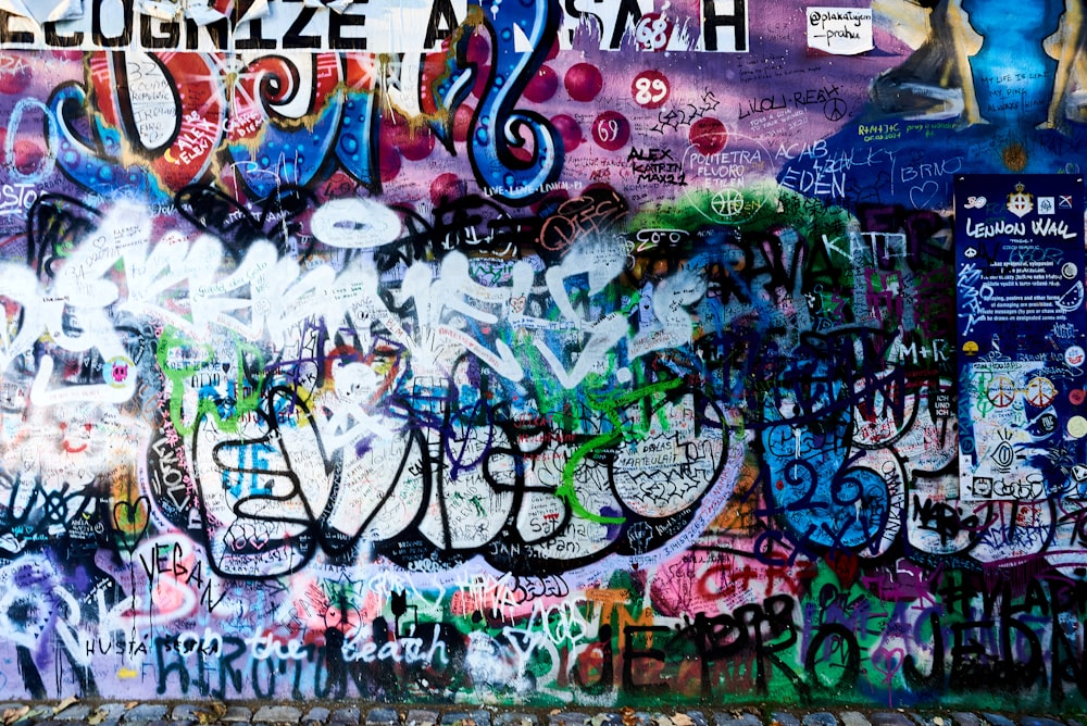 a wall covered in lots of graffiti next to a sidewalk