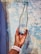 A hand is holding a clear glass bottle with a blue cap. The bottle features a label that reads 'Mayers Natural Spring Water.' The background consists of a textured surface with a mix of blue and beige tones.