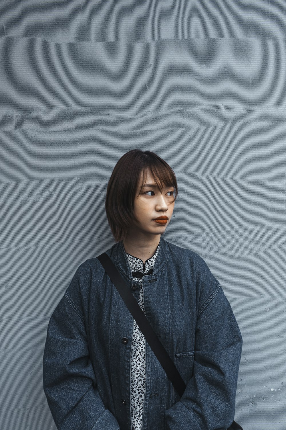 a woman with a black bag standing in front of a gray wall