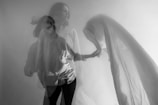 A black and white photograph depicting a double exposure effect of a woman in motion. She is wearing a light-colored blouse and holding or manipulating a flowing piece of fabric. The overlapping images create a sense of movement and ethereal quality.