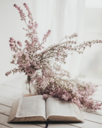 an open book sitting on top of a table next to a bouquet of flowers