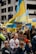A group of people are gathered in a city street, holding and waving Ukrainian flags. They display signs with messages such as 'Stop the War' and 'Stand with Ukraine.' The scene is lively and crowded, with participants wearing various clothing, including traditional Ukrainian attire.
