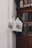A set of canvas tote bags hang by a wooden door, displaying illustrations of a cityscape with the text 'Rothenburg'. The bags are attached to a metal hook and are priced at 3.50, as indicated by a small sign. The scene is softly lit, creating a cozy and quaint atmosphere.