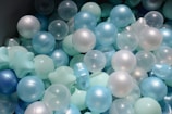 A collection of spherical and star-shaped plastic balls in various shades of blue, white, and translucent colors. They appear to be part of a ball pit, often used in children's play areas.
