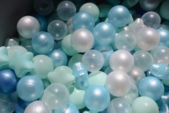 A collection of spherical and star-shaped plastic balls in various shades of blue, white, and translucent colors. They appear to be part of a ball pit, often used in children's play areas.