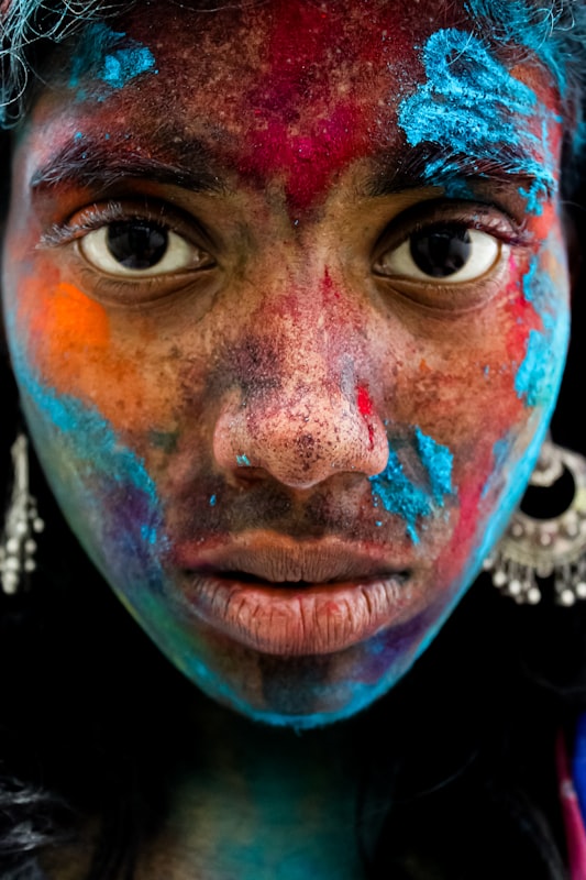 Woman's face covered in blue and orange powder during Holi. Photo by Anjali Lokhande on Unsplash.