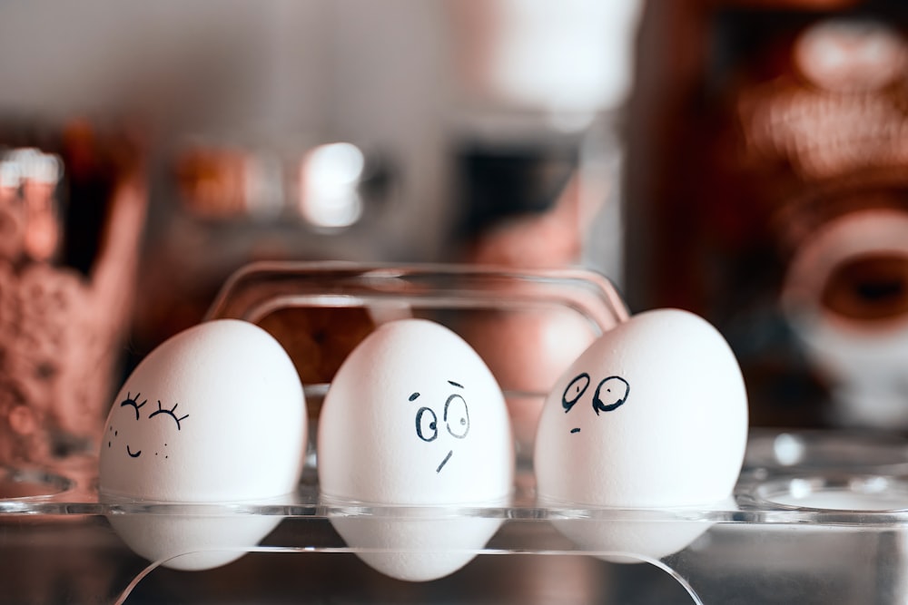 trois œufs avec des visages dessinés sur eux dans un carton
