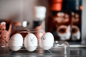 three eggs with faces drawn on them in a plastic container