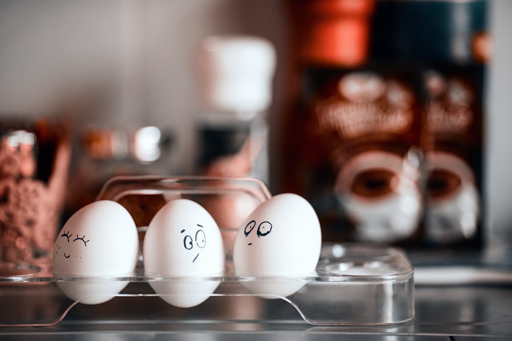 trois œufs avec des visages dessinés dessus dans un récipient en plastique