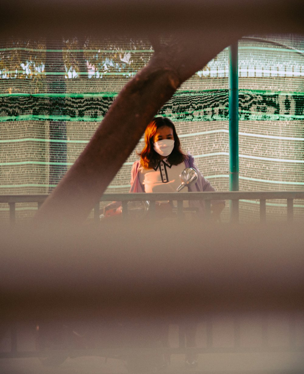 a woman wearing a face mask standing in front of a fence