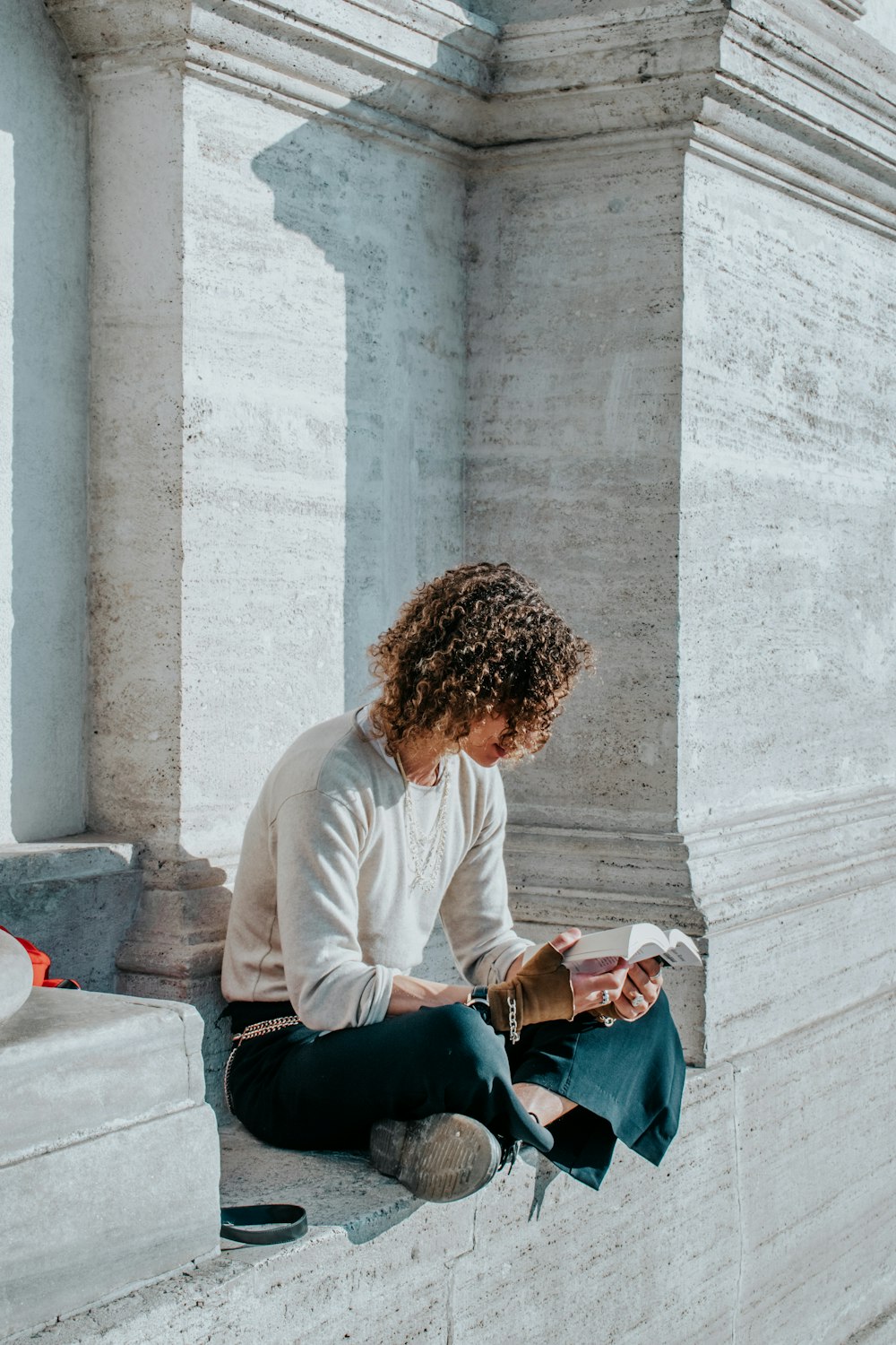 a woman sitting on a ledge reading a book