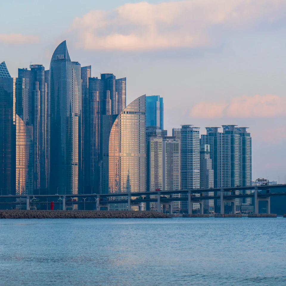 Cityscape with modern skyscraper and bridge spanning across large body of water in foreground