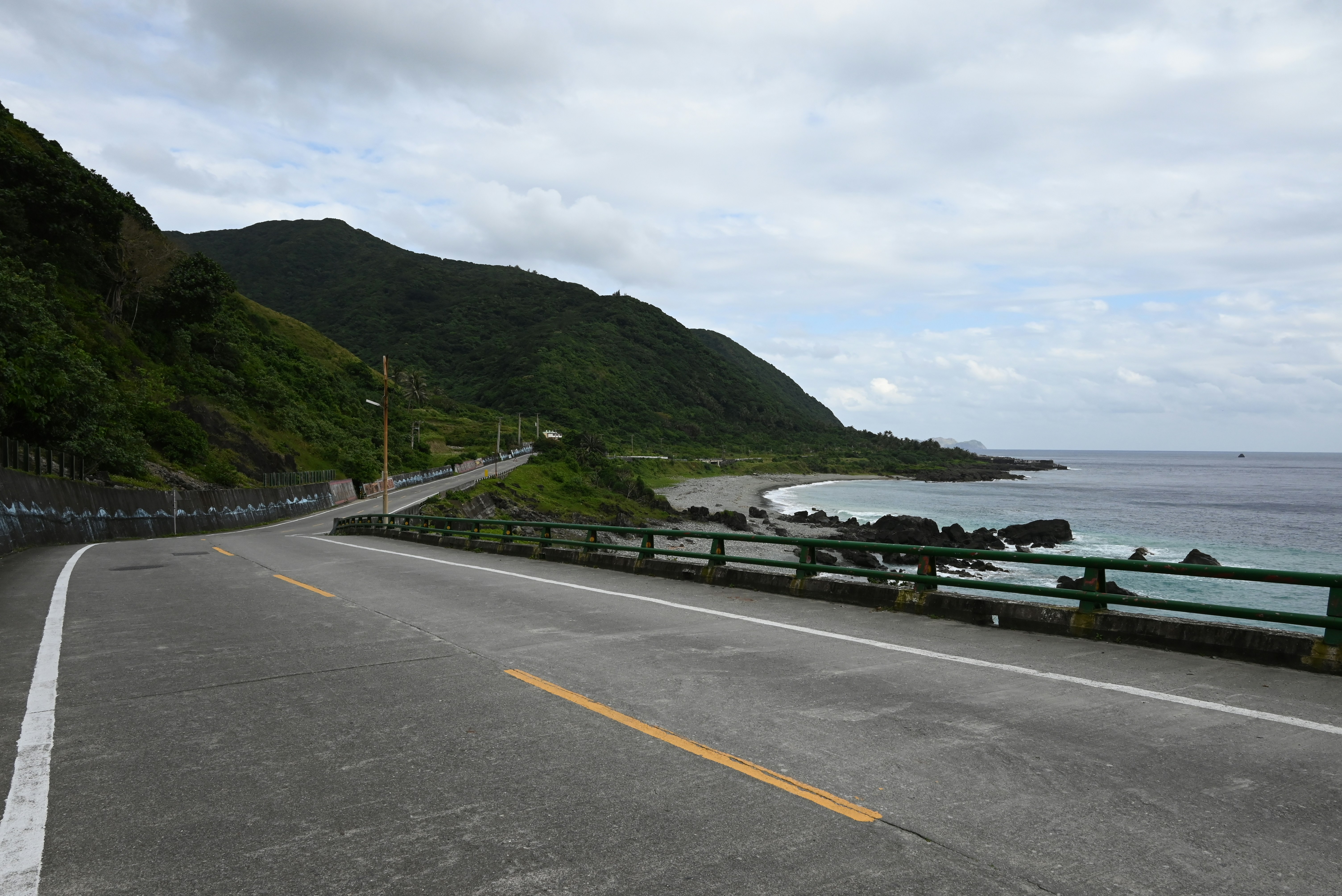 an empty road next to the ocean on a cloudy day