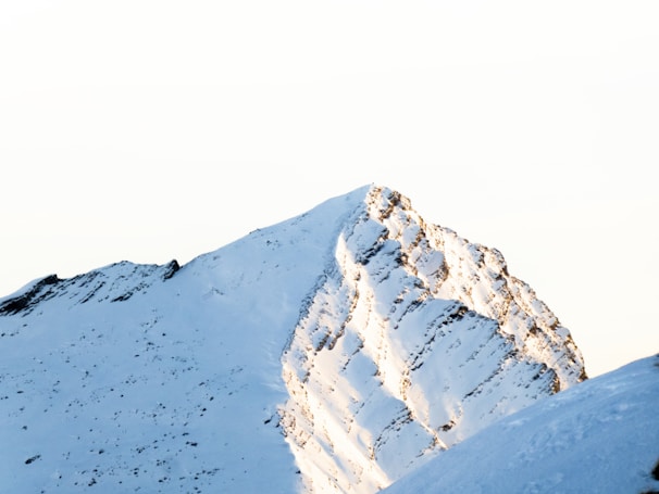 A mountain peak dusted with snow, glowing softly in the early morning light.