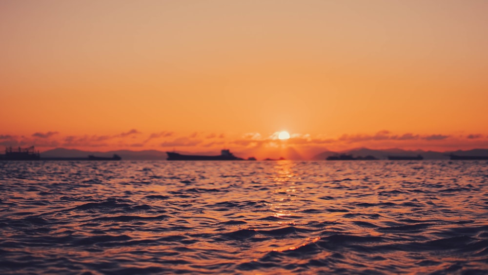 a sunset over the ocean with ships in the distance