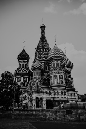 A majestic building with ornate, detailed architecture featuring onion-shaped domes. The structure includes intricate patterns and a combination of sharp and rounded elements. The architecture shows influence from Eastern European styles, noticeable in the elaborate and colorful designs, although presented in grayscale.