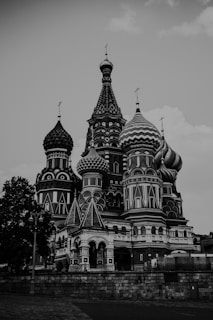 A majestic building with ornate, detailed architecture featuring onion-shaped domes. The structure includes intricate patterns and a combination of sharp and rounded elements. The architecture shows influence from Eastern European styles, noticeable in the elaborate and colorful designs, although presented in grayscale.