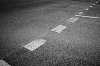 A section of asphalt road is visible with marked white dashed lines indicating separation lanes. The surface has a coarse texture and appears slightly worn.