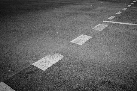 A section of asphalt road is visible with marked white dashed lines indicating separation lanes. The surface has a coarse texture and appears slightly worn.