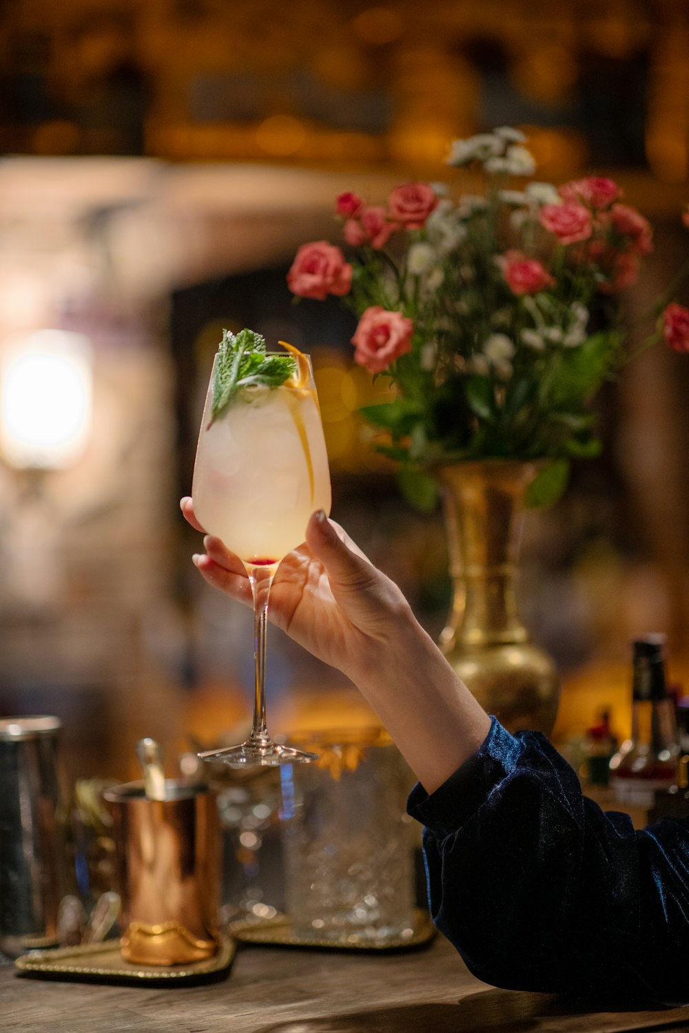 a person holding a wine glass in front of a vase of flowers