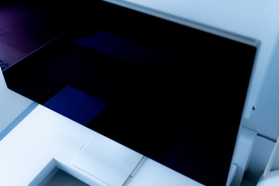 A modern, angular architectural structure with sleek lines and a minimalist design. The image features a large, dark reflective surface, likely a window or screen, surrounded by light-colored walls and geometric shapes.