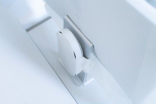 A white, sleek, vertical gaming console placed beside a large, slim monitor. The setting exudes minimalism with a focus on modern technology design.