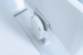 A white, sleek, vertical gaming console placed beside a large, slim monitor. The setting exudes minimalism with a focus on modern technology design.