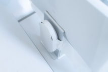 A white, sleek, vertical gaming console placed beside a large, slim monitor. The setting exudes minimalism with a focus on modern technology design.