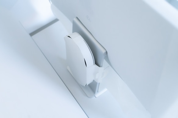 A white, sleek, vertical gaming console placed beside a large, slim monitor. The setting exudes minimalism with a focus on modern technology design.