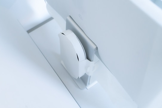 A white, sleek, vertical gaming console placed beside a large, slim monitor. The setting exudes minimalism with a focus on modern technology design.