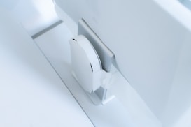 A white, sleek, vertical gaming console placed beside a large, slim monitor. The setting exudes minimalism with a focus on modern technology design.