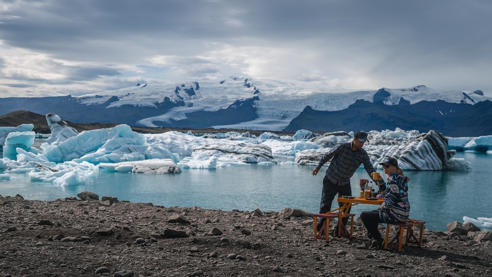 a man and a woman sitting at a table in front of a glacier