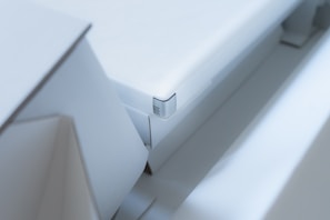 A close-up view of a modern, minimalist white object with sharp edges and geometric shapes. The design is sleek and clean with a focus on angular forms and subtle details.