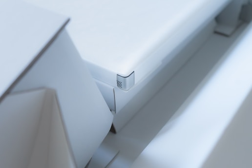 A close-up view of a modern, minimalist white object with sharp edges and geometric shapes. The design is sleek and clean with a focus on angular forms and subtle details.