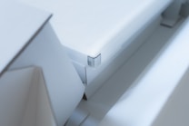 A close-up view of a modern, minimalist white object with sharp edges and geometric shapes. The design is sleek and clean with a focus on angular forms and subtle details.