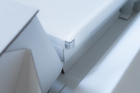 A close-up view of a modern, minimalist white object with sharp edges and geometric shapes. The design is sleek and clean with a focus on angular forms and subtle details.